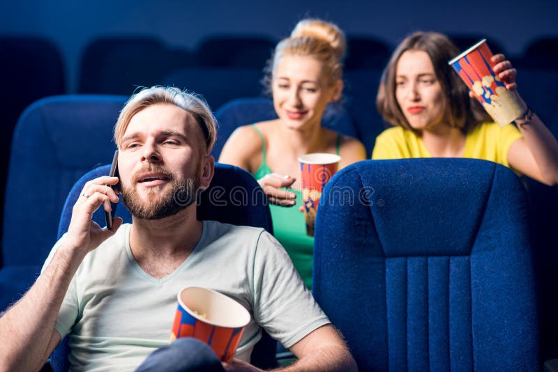 Rude men talking with phone disturbing women on the back seats in the cinema. Rude men talking with phone disturbing women on the back seats in the cinema