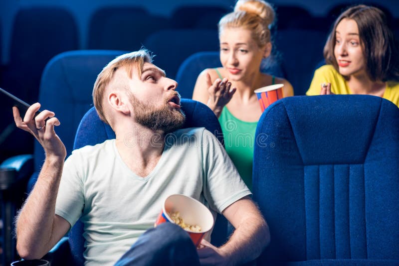 Rude men talking with phone disturbing women on the back seats in the cinema. Rude men talking with phone disturbing women on the back seats in the cinema