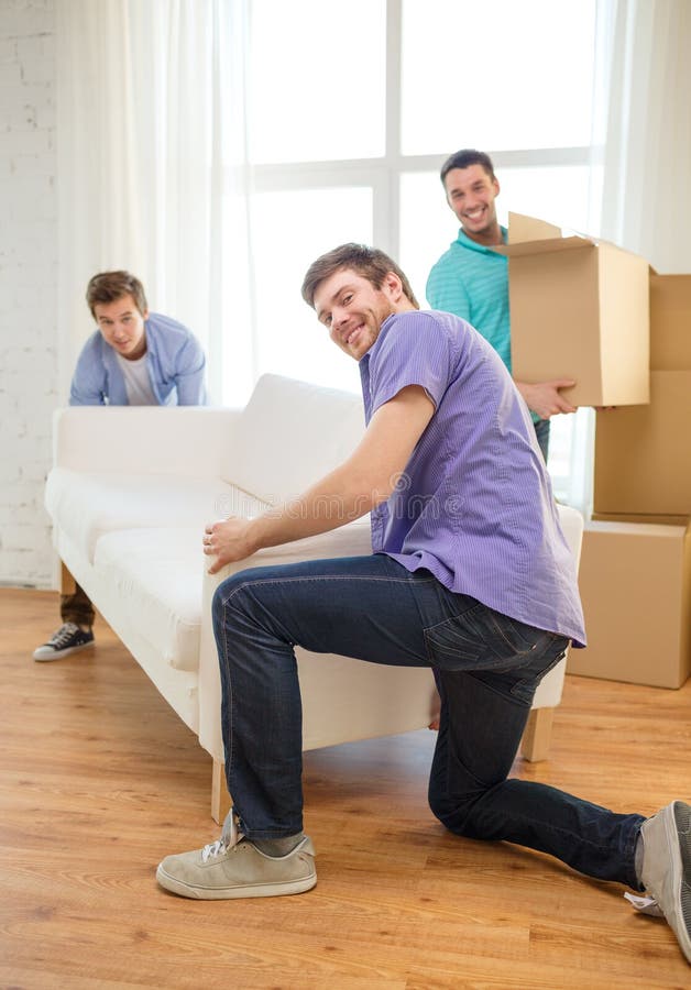 Amis de sourire avec le sofa et les boîtes à la nouvelle maison image libre de droits Amis de sourire avec le sofa et les boîtes à la nouvelle maison image libre de droits
