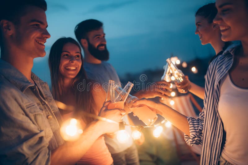 Amis heureux avec des boissons grillant? la partie de dessus de toit la nuit photo libre de droits