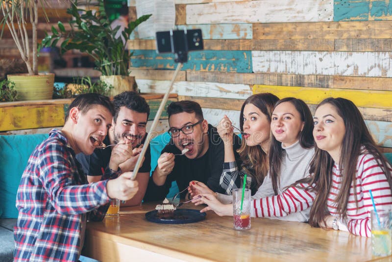 Amis heureux ayant l'amusement prenant ensemble le selfie tout en partageant le gâteau de chocolat image libre de droits Amis heureux ayant l'amusement prenant ensemble le selfie tout en partageant le gâteau de chocolat image libre de droits