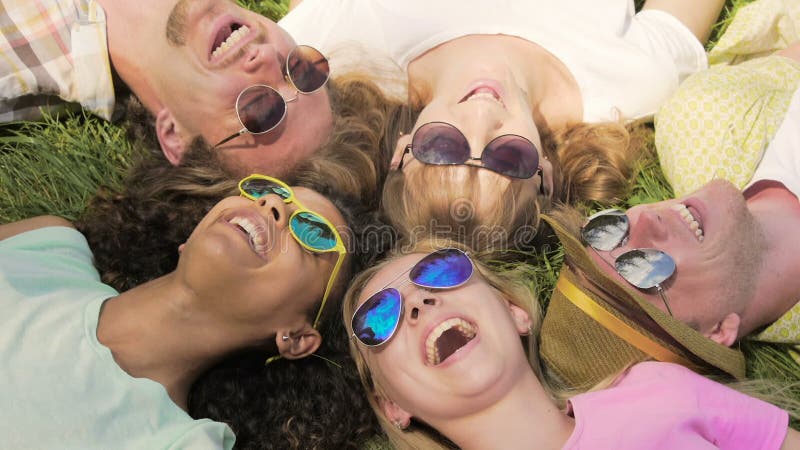 Amis heureux dans l'herbe menteuse de lunettes de soleil, parlant et riant, partageant des secrets clips vidéos