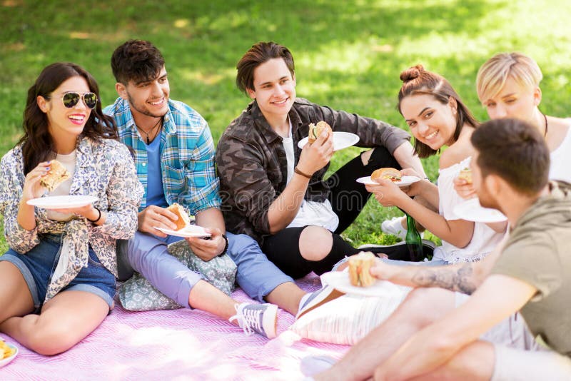 Amis heureux mangeant des sandwichs au pique-nique d'été photo libre de droits Amis heureux mangeant des sandwichs au pique-nique d'été photo libre de droits