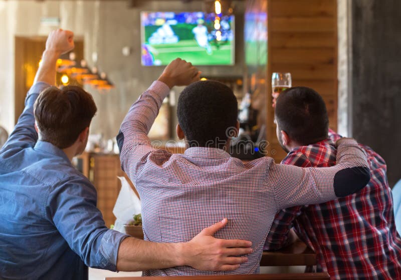 Amis masculins observant le match de football à la TV dans la barre photographie stock Amis masculins observant le match de football à la TV dans la barre photographie stock