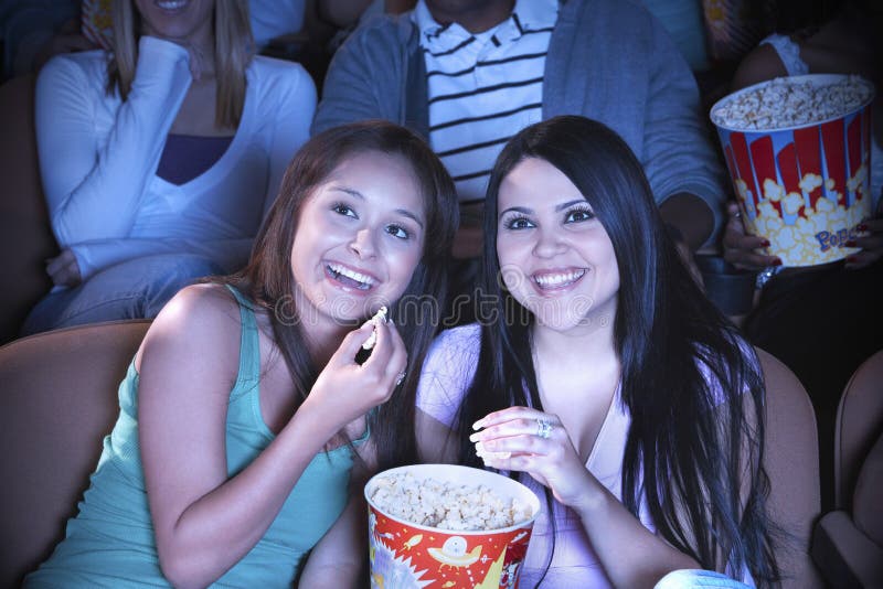 Young friends eating popcorn while watching film in movie theater. Young friends eating popcorn while watching film in movie theater