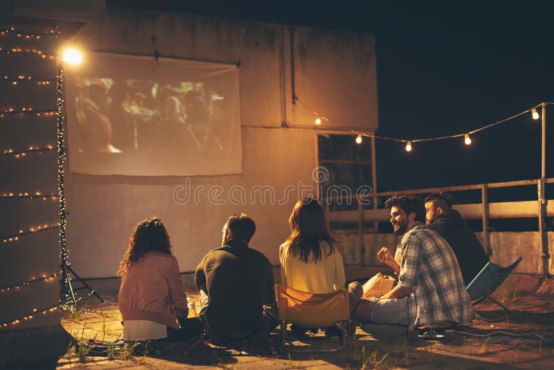Amis observant un film sur une terrasse de construction de dessus de toit photographie stock libre de droits Amis observant un film sur une terrasse de construction de dessus de toit photographie stock libre de droits