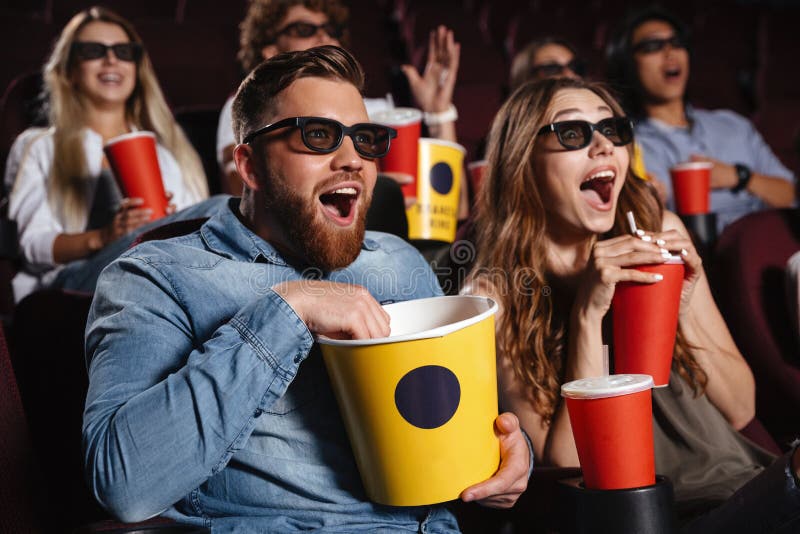 Image of laughing friends sitting in cinema watch film eating popcorn and drinking aerated sweet water. Image of laughing friends sitting in cinema watch film eating popcorn and drinking aerated sweet water.