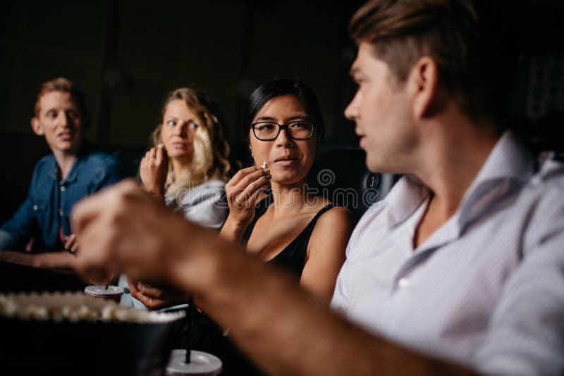 Group of friends sitting in multiplex movie theater and talking. Young people in cinema with popcorn. Group of friends sitting in multiplex movie theater and talking. Young people in cinema with popcorn.