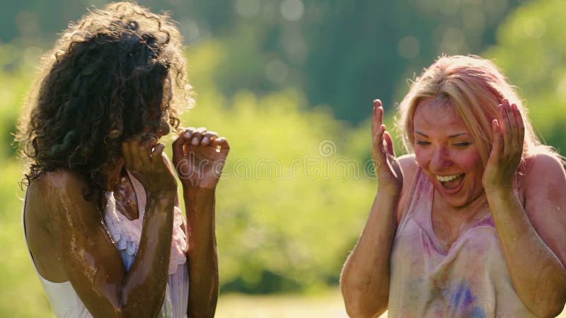 Amis éclaboussant l'eau sur deux jeunes femmes excitées couvertes dans la poudre de couleur banque de vidéos