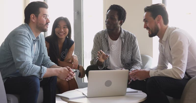 Amistoso y feliz equipo de negocios multiétnico hablando con el portátil almacen de video