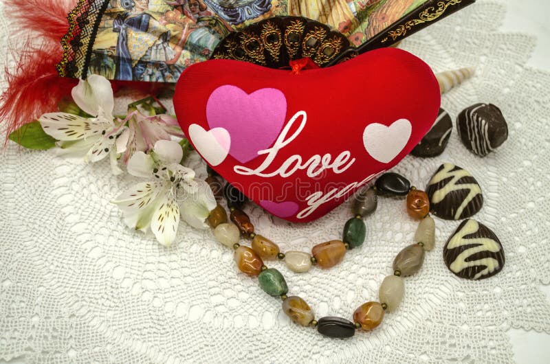 Amivi su cuore, sulle perle, sul cioccolato, sul fan e sui fiori rossi su un tovagliolo openwork bianco immagini stock libere da diritti Amivi su cuore, sulle perle, sul cioccolato, sul fan e sui fiori rossi su un tovagliolo openwork bianco immagini stock libere da diritti
