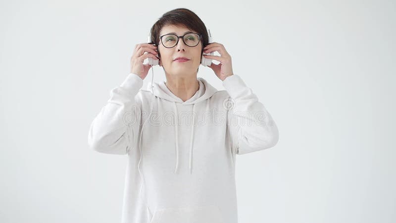Amor para o conceito da m?sica A mulher madura flui a música nos fones de ouvido em um fundo branco video estoque Amor para o conceito da m?sica A mulher madura flui a música nos fones de ouvido em um fundo branco video estoque