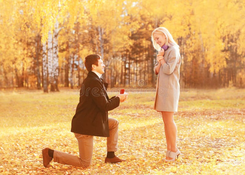 Amor, relaciones, concepto del compromiso y de la boda - el hombre arrodillado propone a una mujer para casarse, anillo rojo de l fotografía de archivo libre de regalías Amor, relaciones, concepto del compromiso y de la boda - el hombre arrodillado propone a una mujer para casarse, anillo rojo de l fotografía de archivo libre de regalías