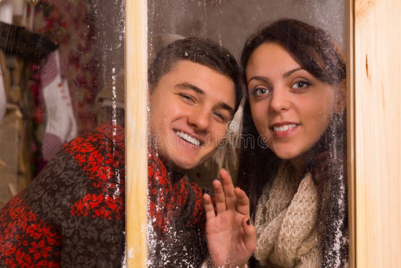Amores jovenes que sonríen detrás de la ventana de cristal fotos de archivo Amores jovenes que sonríen detrás de la ventana de cristal fotos de archivo