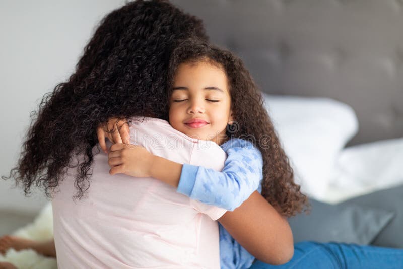 Amorosa menina negra em vestir casual abraçando sua mãe na cama em casa. conceito de relações familiares fortes