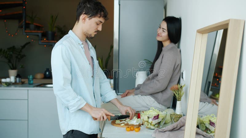 Amoroso marido cocinando comida y alimentando a la esposa hermosa mujer asiática en la cocina en el apartamento