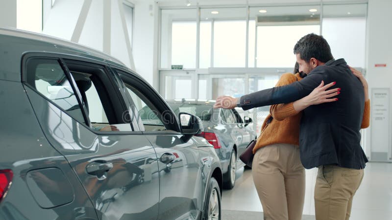 Amoroso marido dando coche a esposa amada como una sorpresa en sala de exposición de motor