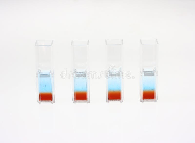 Four quartz cuvettes that contain two liquid phases for a biotechnological colour comparative analysis on a white background. Biological samples can be observed in the blue and red/brown liquids. Four quartz cuvettes that contain two liquid phases for a biotechnological colour comparative analysis on a white background. Biological samples can be observed in the blue and red/brown liquids.