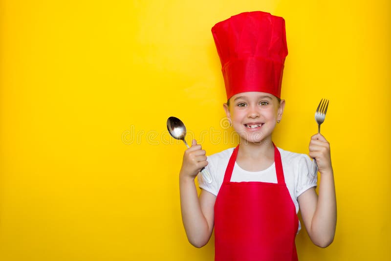 Ampia ragazza sorridente nel vestito di un cuoco unico rosso che tiene un cucchiaio e una forchetta su fondo giallo con lo spazio fotografia stock libera da diritti Ampia ragazza sorridente nel vestito di un cuoco unico rosso che tiene un cucchiaio e una forchetta su fondo giallo con lo spazio fotografia stock libera da diritti