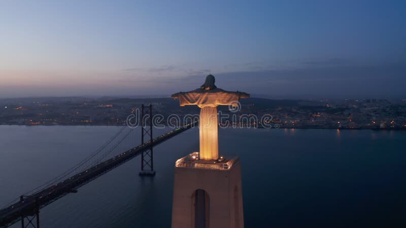 Amplia órbita aérea del gran monumento alto del santuario de cristo rei con luces y el ponte rojo 25 de abril bridge almacen de video