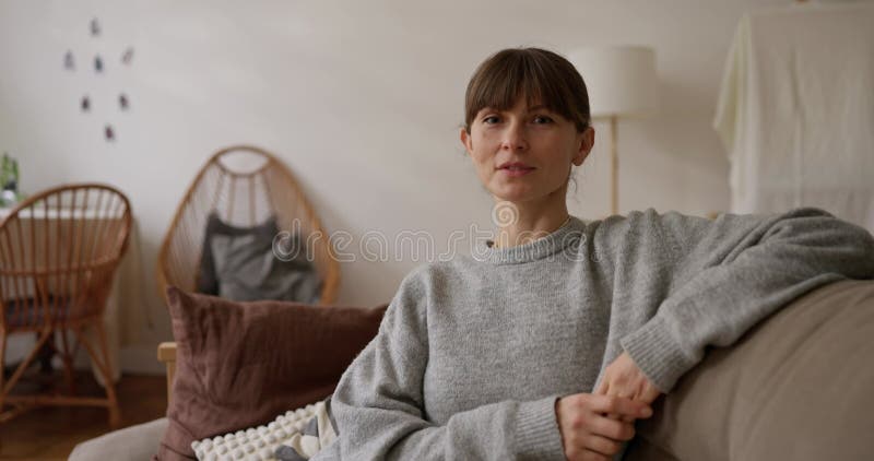 Ampliar el retrato de una chica con ojos azules en un suéter posando sobre un sofá en una acogedora sala luminosa. Retrato de la m almacen de video