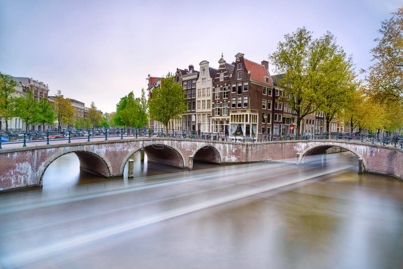 Amsterdam. Bridge and water canal. Boat light trail on sunset. Holland or Netherlands.