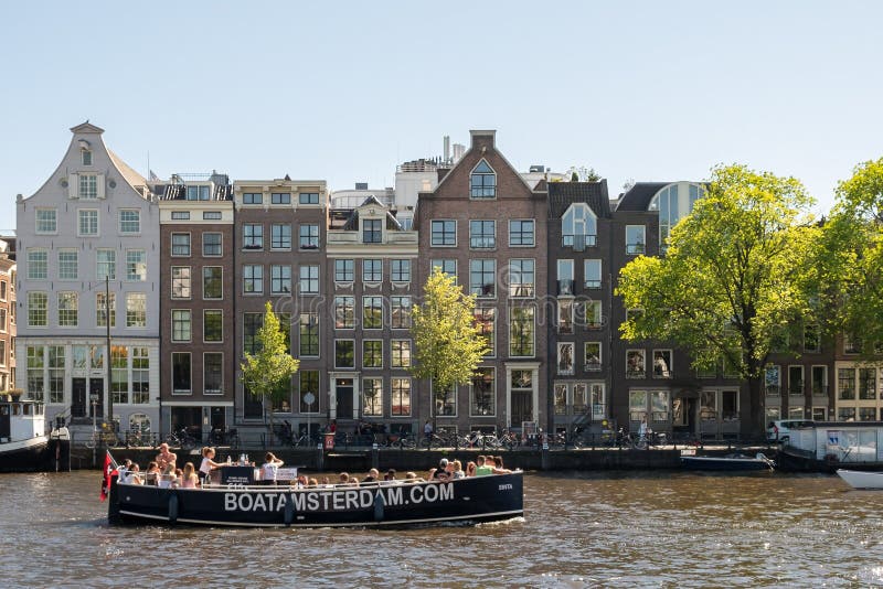 Amsterdam Nederländerna, May, 2018: Amstel flodstrand på en solig dag med typiska hus och fartyg längs floden royaltyfri foto Amsterdam Nederländerna, May, 2018: Amstel flodstrand på en solig dag med typiska hus och fartyg längs floden royaltyfri foto