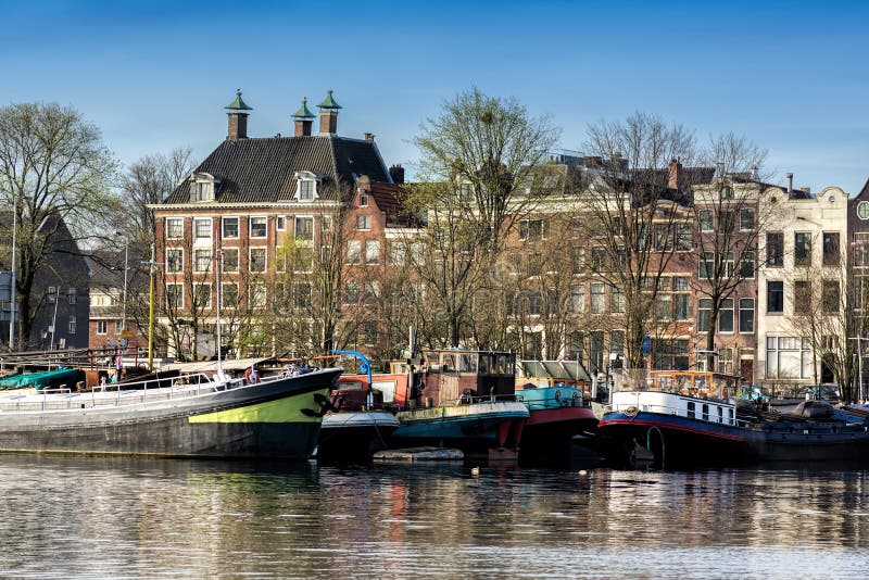 AMSTERDAM SOM ÄR NEDERLÄNDSK - APRIL 10, 2018: Amsterdam cityscape med typiska holländska hus och fartyg från Oosterdoken i Nethe royaltyfria foton AMSTERDAM SOM ÄR NEDERLÄNDSK - APRIL 10, 2018: Amsterdam cityscape med typiska holländska hus och fartyg från Oosterdoken i Nethe royaltyfria foton