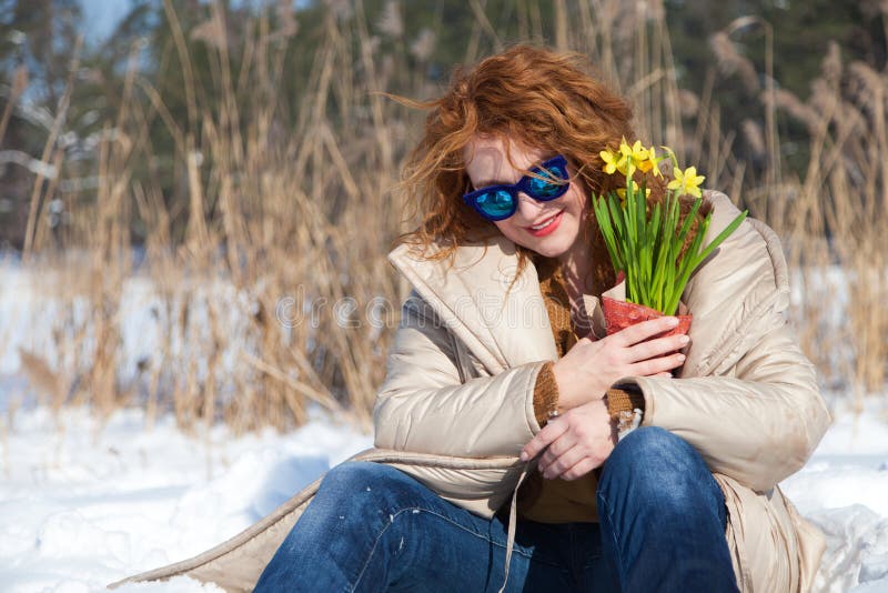 Amused charming woman with blue sunglasses resting in snow while looking down stock photo Amused charming woman with blue sunglasses resting in snow while looking down stock photo