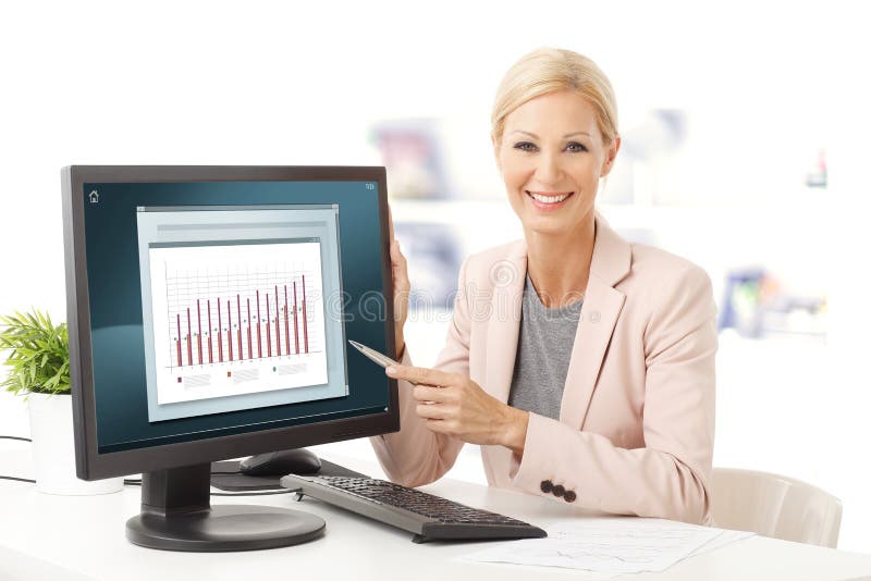 Portrait of financial assistant sitting at office. Young businesswoman sitting at desk and points the monitor which diagram is displayed on the screen. Portrait of financial assistant sitting at office. Young businesswoman sitting at desk and points the monitor which diagram is displayed on the screen.