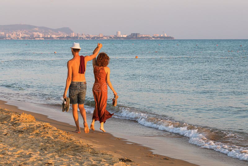 ANAPA, RYSSLAND - JULI 04 JULI 2019: Ett par turister som går längs kvällstranden arkivbilder ANAPA, RYSSLAND - JULI 04 JULI 2019: Ett par turister som går längs kvällstranden arkivbilder