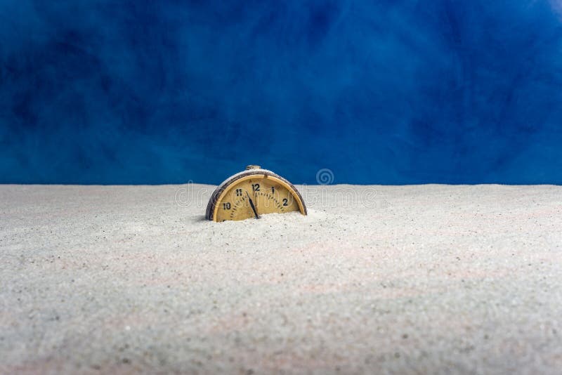 Ancient alarm clock on sand and blue background