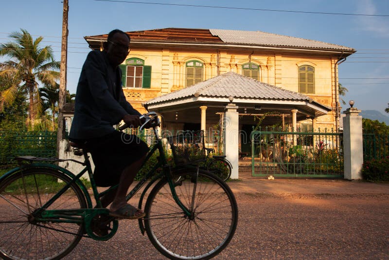 Ancient and beautiful, Laos men riding bicycle past old french colonial house in the evening. Champasak, Laos