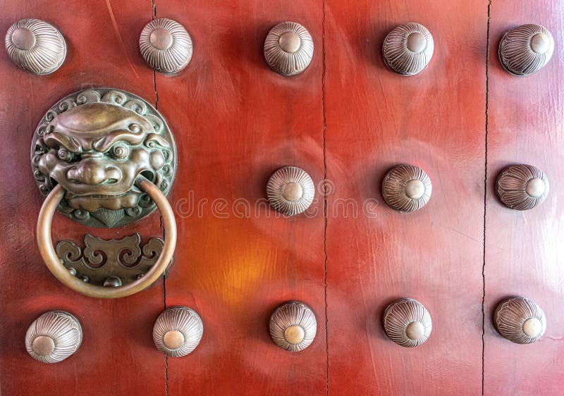 Ancient red wooden door decorated with bronze casting bas relief into Chinese lion face holding a ring-shaped handle in the mouth stock image Ancient red wooden door decorated with bronze casting bas relief into Chinese lion face holding a ring-shaped handle in the mouth stock image