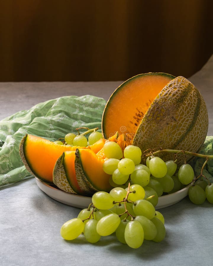 Ancora vita con il cibo. Un melone fresco d'arancia è affettato su un piatto e un sacco di uva bianca immagini stock