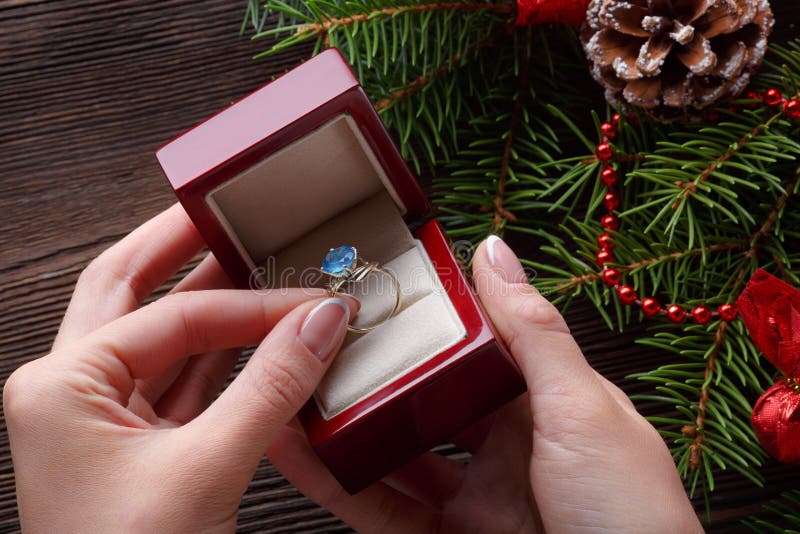 Anello di fidanzamento in mani femminili fra le decorazioni di Natale su fondo di legno fotografie stock libere da diritti Anello di fidanzamento in mani femminili fra le decorazioni di Natale su fondo di legno fotografie stock libere da diritti