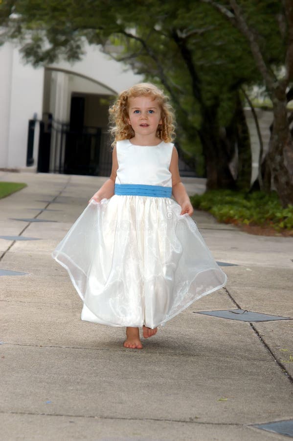 Angelic child with blonde ringlets holds her gown and runs down a garden path. She is wearing a white gown with bright blue sash. Angelic child with blonde ringlets holds her gown and runs down a garden path. She is wearing a white gown with bright blue sash.