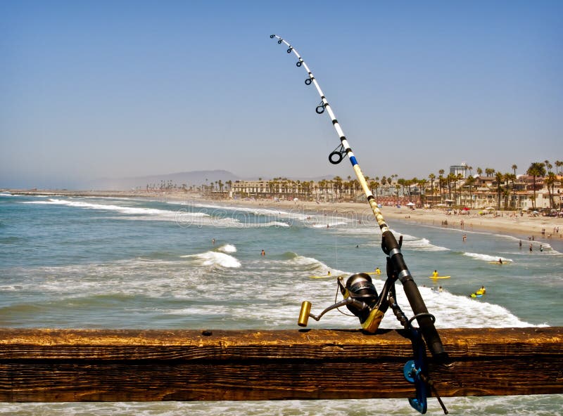 Fishing rod balanced on an ocean pier in Oceanside, southern California, on the west coast of the United States, to hook a fish for dinner, with the ocean, beach, buildings and palm trees in the background. Fishing rod balanced on an ocean pier in Oceanside, southern California, on the west coast of the United States, to hook a fish for dinner, with the ocean, beach, buildings and palm trees in the background.