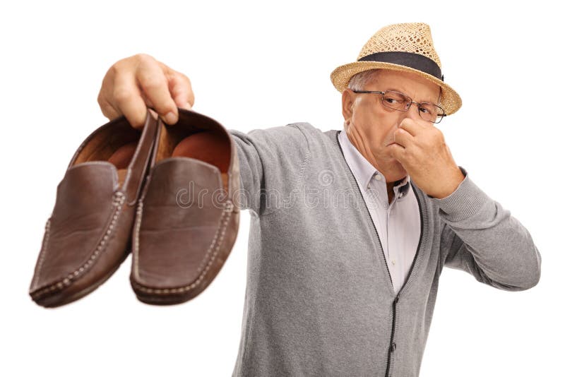 Disgusted senior holding a pair of stinky shoes isolated on white background. Disgusted senior holding a pair of stinky shoes isolated on white background