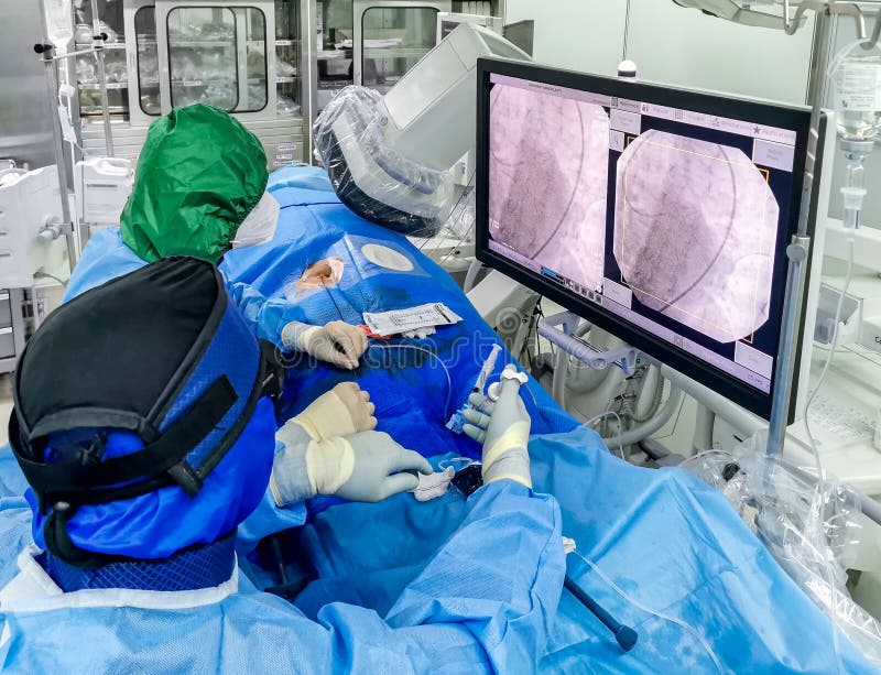 This shot shows an ongoing emergency coronary angioplasty procedure perform in a cardiac catheterization laboratory during COVID. The medical staff is in full PPE. This shot shows an ongoing emergency coronary angioplasty procedure perform in a cardiac catheterization laboratory during COVID. The medical staff is in full PPE