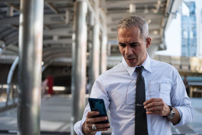 Shocked middle-age, 40s to 50s, businessman take off eyeglasses and read bad business project news from smartphone in modern city. Serious, Stressed, Anxious, surprised old working man, account, adult, aged, amazed, app, astonished, attention, background, cellphone, company, corporate, disbelief, dumbfounded, email, emotion, employee, expression, fees, gossip, guy, information, insider, internet, media, message, mobile, office, omg, person, picture, price, private, problem, reading, rumor, sms, social, stupid, technology, watching. Shocked middle-age, 40s to 50s, businessman take off eyeglasses and read bad business project news from smartphone in modern city. Serious, Stressed, Anxious, surprised old working man, account, adult, aged, amazed, app, astonished, attention, background, cellphone, company, corporate, disbelief, dumbfounded, email, emotion, employee, expression, fees, gossip, guy, information, insider, internet, media, message, mobile, office, omg, person, picture, price, private, problem, reading, rumor, sms, social, stupid, technology, watching