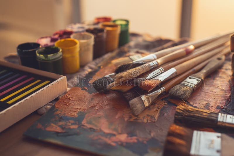 Angle view photo of palette with mixed oil paints, gouache, crayons and paintbrushes set in art studio.