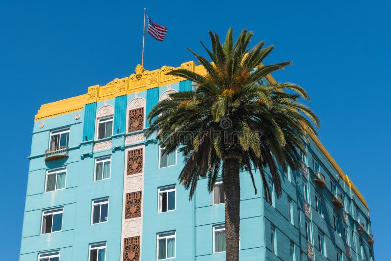 Angled front and side view of a blue art deco style building with yellow trim with an American flag on the rooftop and a palm tree stock photo Angled front and side view of a blue art deco style building with yellow trim with an American flag on the rooftop and a palm tree stock photo