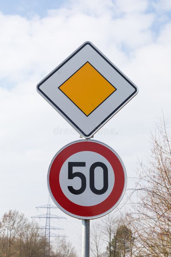 A vertical low angle shot of the traffic sign for priority road and speed limit sign on a post. A vertical low angle shot of the traffic sign for priority road and speed limit sign on a post