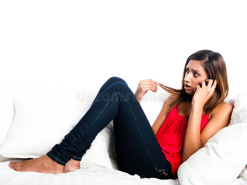 Beautiful upset asian teenage girl lying on the sofa, listening on the phone and playing with hair. Beautiful upset asian teenage girl lying on the sofa, listening on the phone and playing with hair