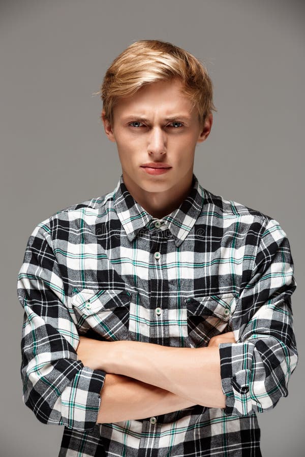 Angry blond handsome young man wearing casual plaid shirt with hands crossed on chest looking at camera, copy space