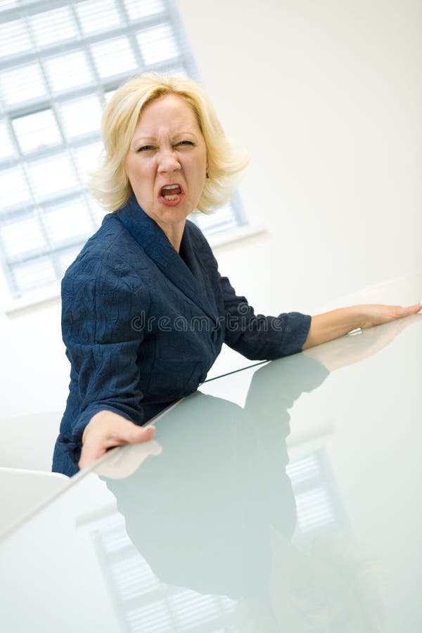 Portrait of middle aged businesswoman seated at office table shouting with anger. Portrait of middle aged businesswoman seated at office table shouting with anger.