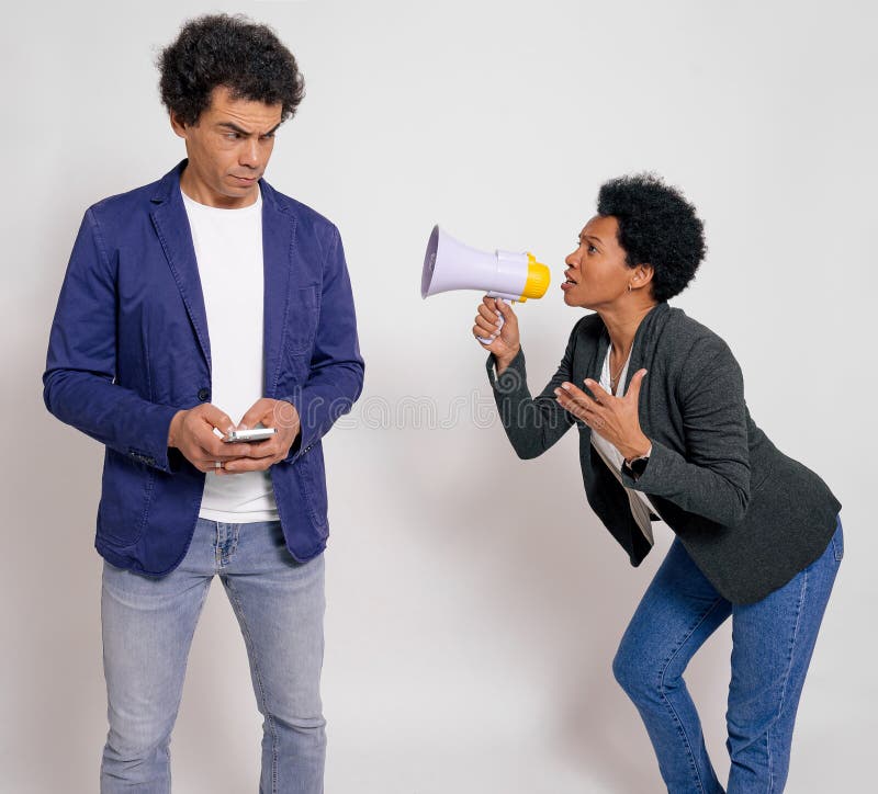 Angry businesswoman with megaphone yelling at male coworker using mobile phone on white background.