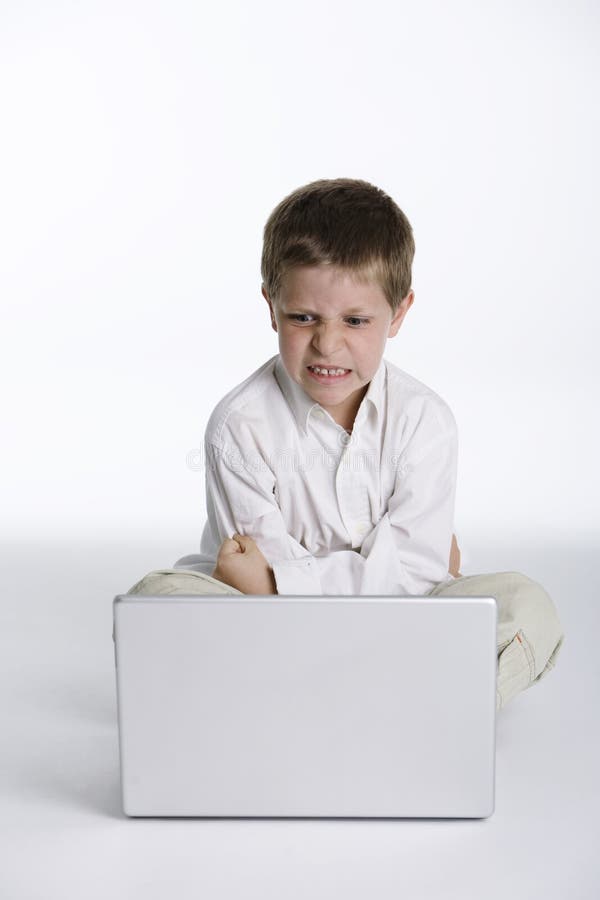 Preschooler child sitting in front of a laptop computer with an angry expression. Preschooler child sitting in front of a laptop computer with an angry expression