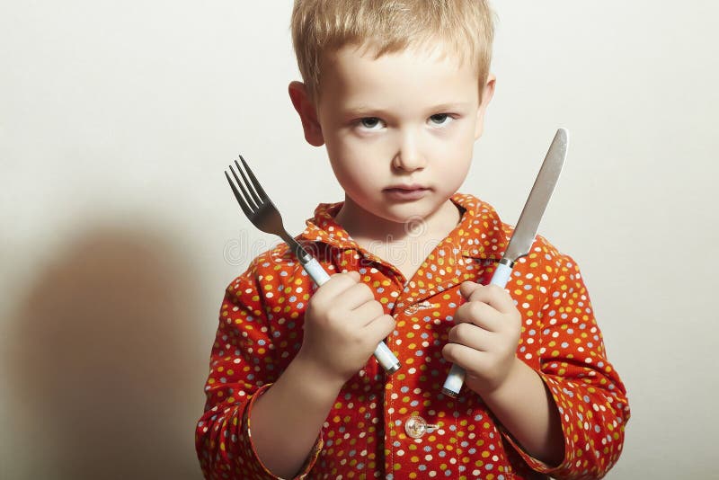 Portrait of Angry child. hungry little boy with Fork and Knife. Food. Want to eat